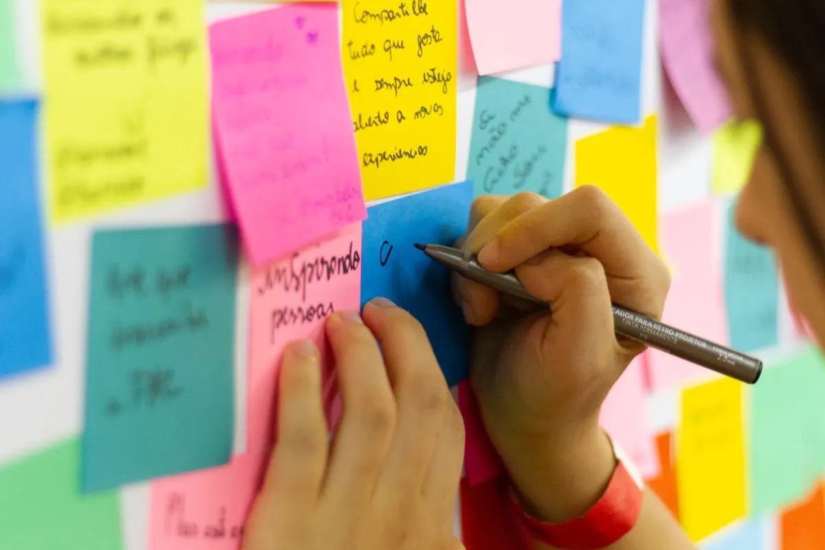 A person writing a note among colorful sticky notes on a shared wall.